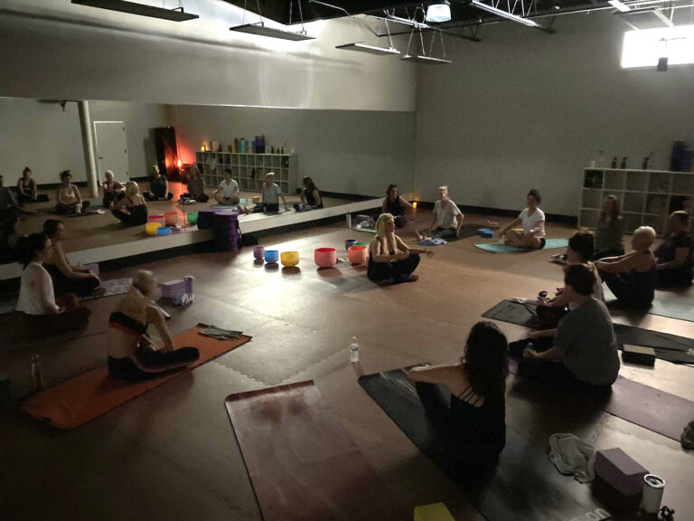 Darkly lite yoga studio, with sound bowl instructor teaching students.